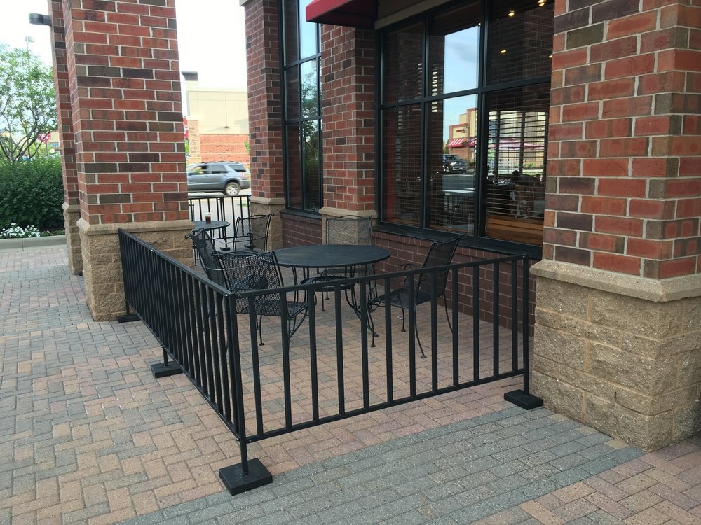 Open rail black metal barrier enclosing an outdoor restaurant patio