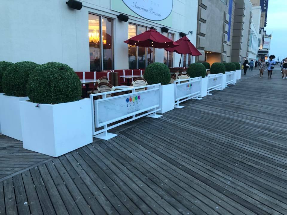 White framed solid-panel sidewalk barriers surrounding restaurant seating